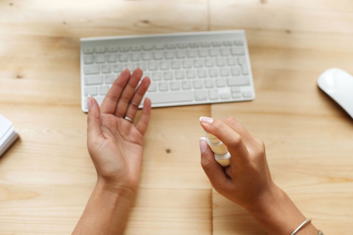 Gloved hands disinfecting an office desk beside a laptop and coffee cup