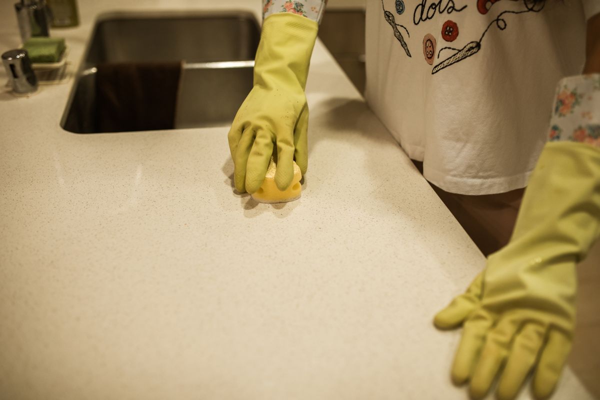Cleaner wiping down a kitchen stovetop in a bright home