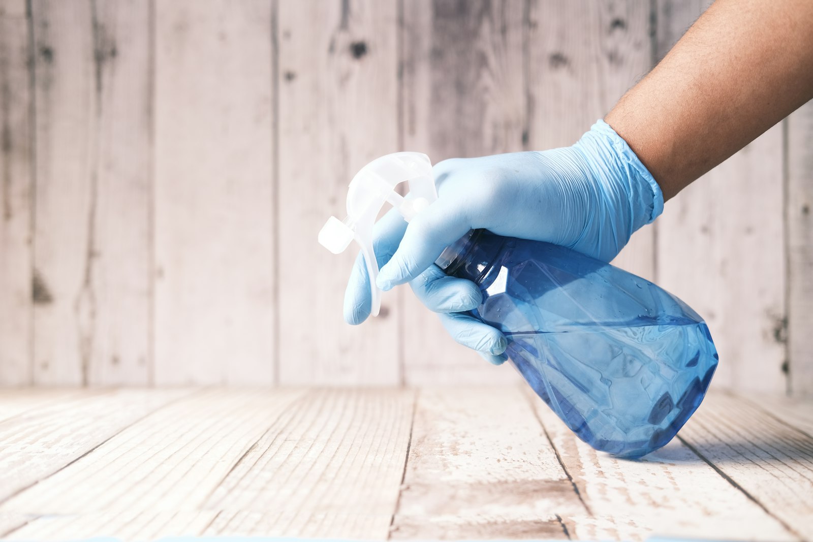 Gloved hand cleaning a surface with a spray bottle